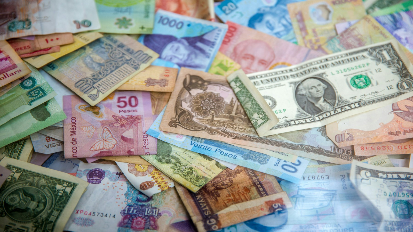 Stack of international paper currency including US dollars on a desk