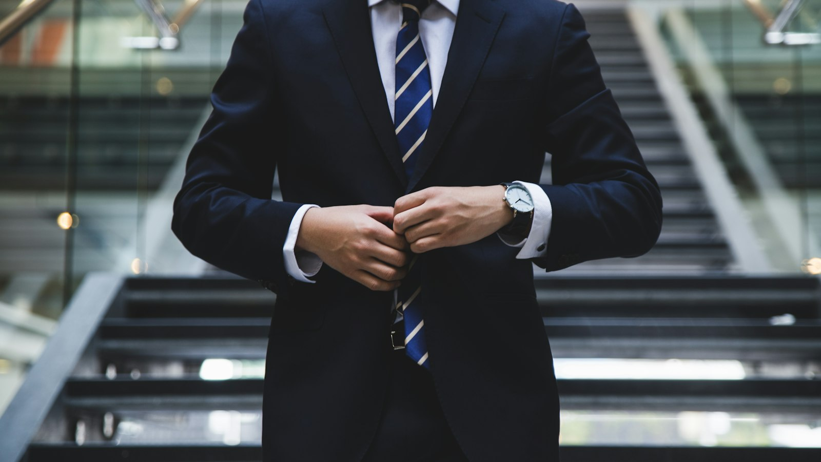 Person in a navy suit adjusting a jacket button in a modern office lobby