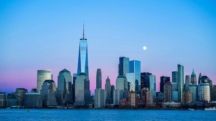 Lower Manhattan skyline at blue hour with One World Trade Center and a full moon