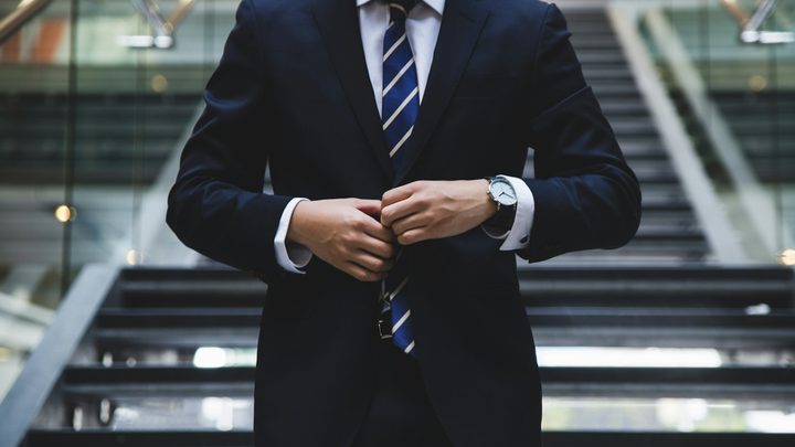 Person in a navy suit adjusting a jacket button in a modern office lobby