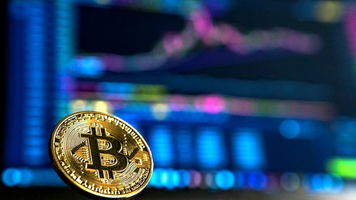 Gold physical Bitcoin coin in sharp focus before glowing trading charts