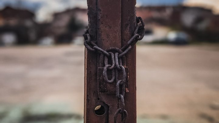 Rusty chain wrapped around a weathered metal post against a blurred background