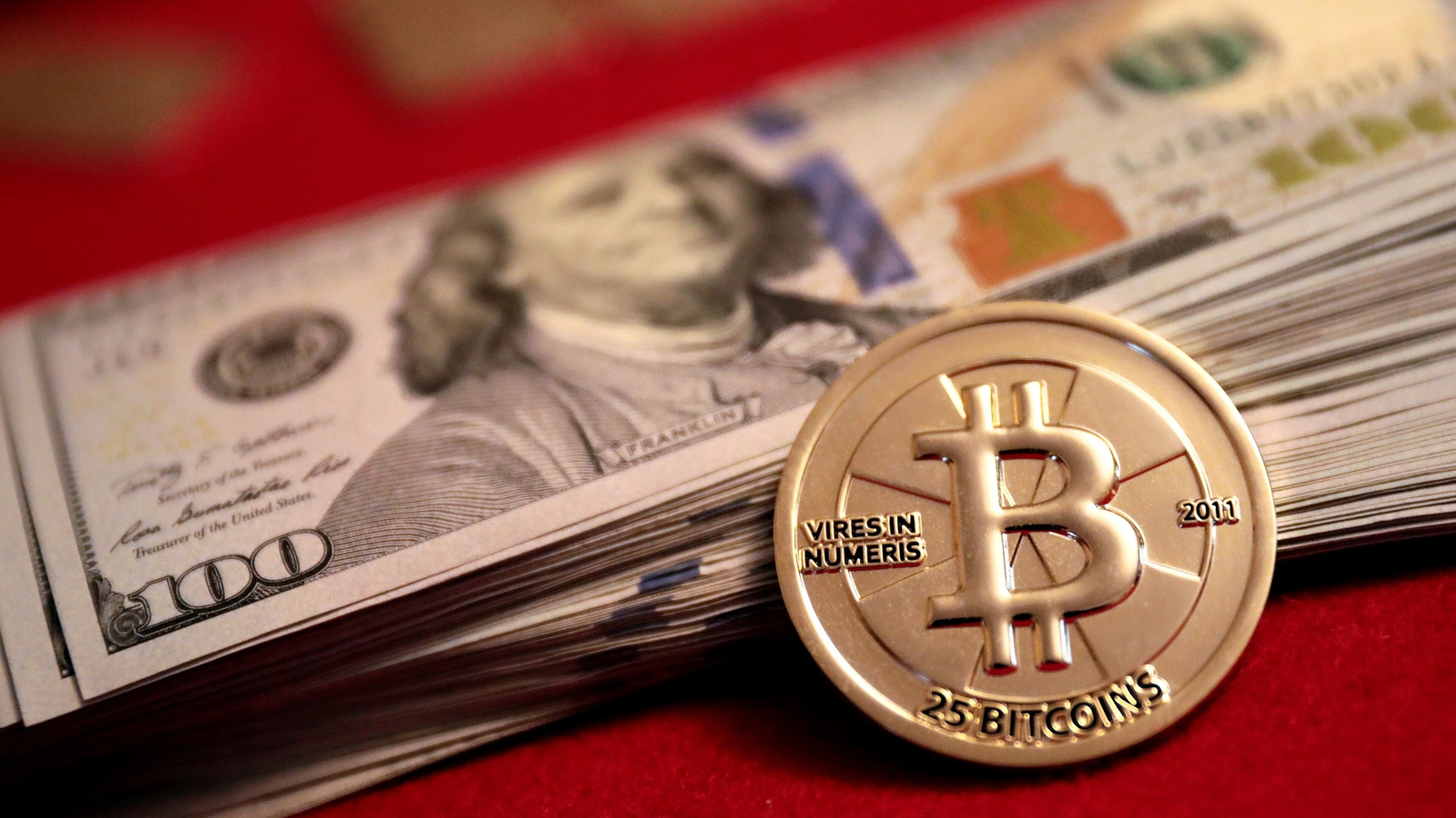 Gold 25-bitcoin Casascius coin resting on a stack of $100 bills
