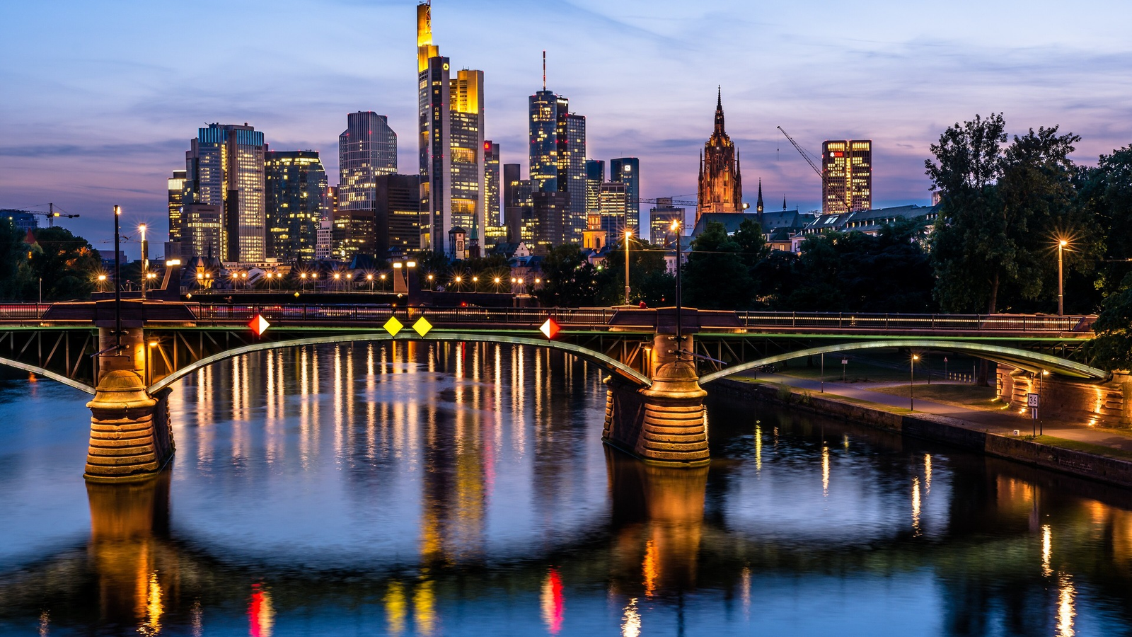 Frankfurt skyline and an illuminated bridge reflected in the Main river at sunset