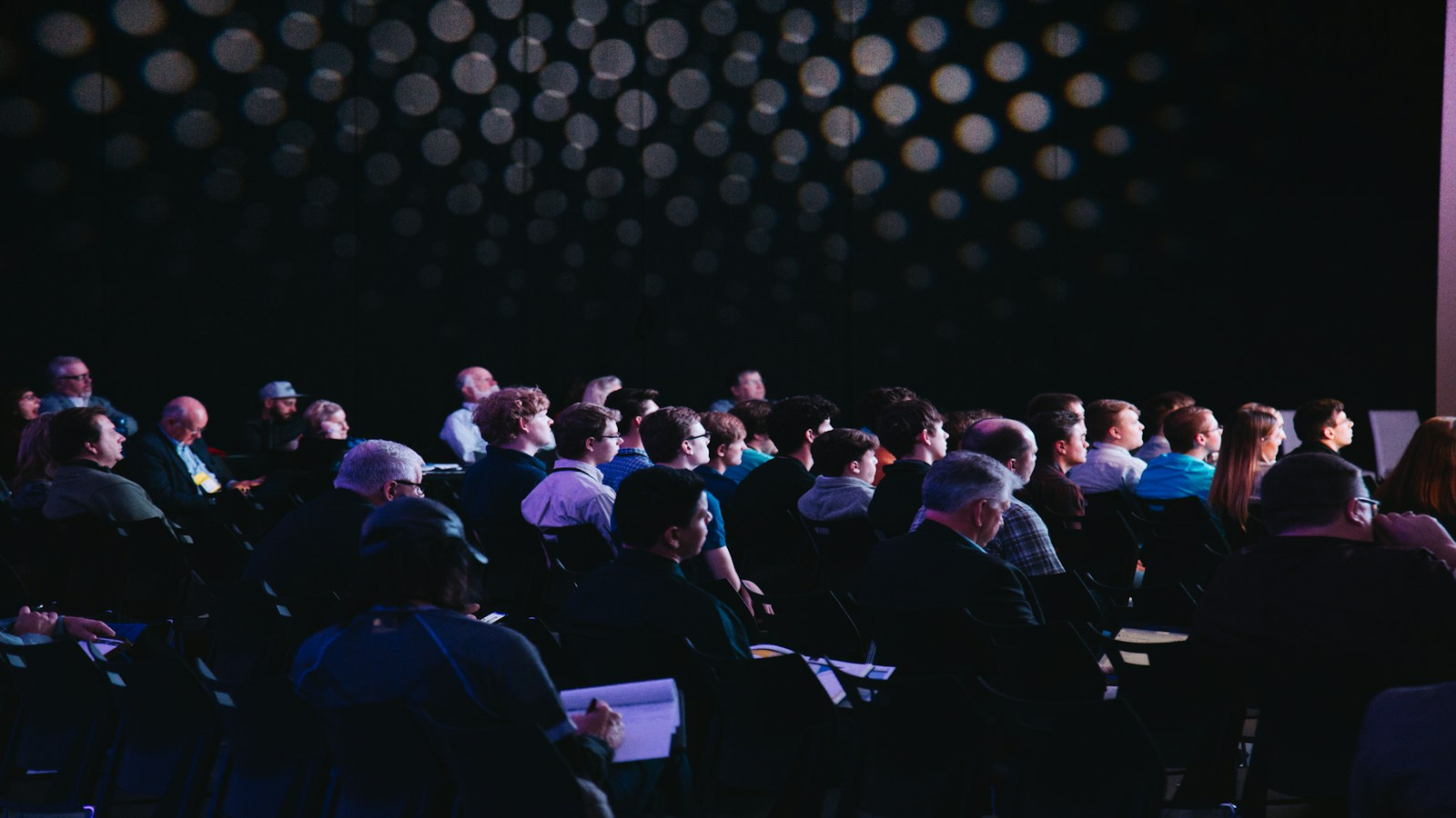 Crowded conference hall audience facing a brightly lit stage
