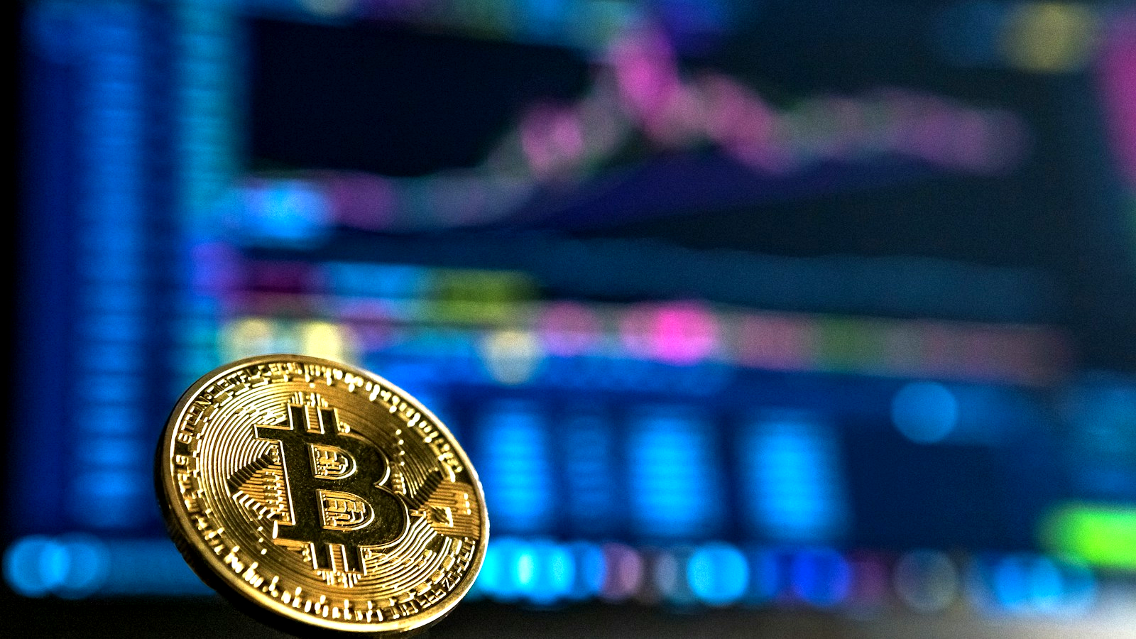 Gold physical Bitcoin coin in sharp focus before glowing trading charts