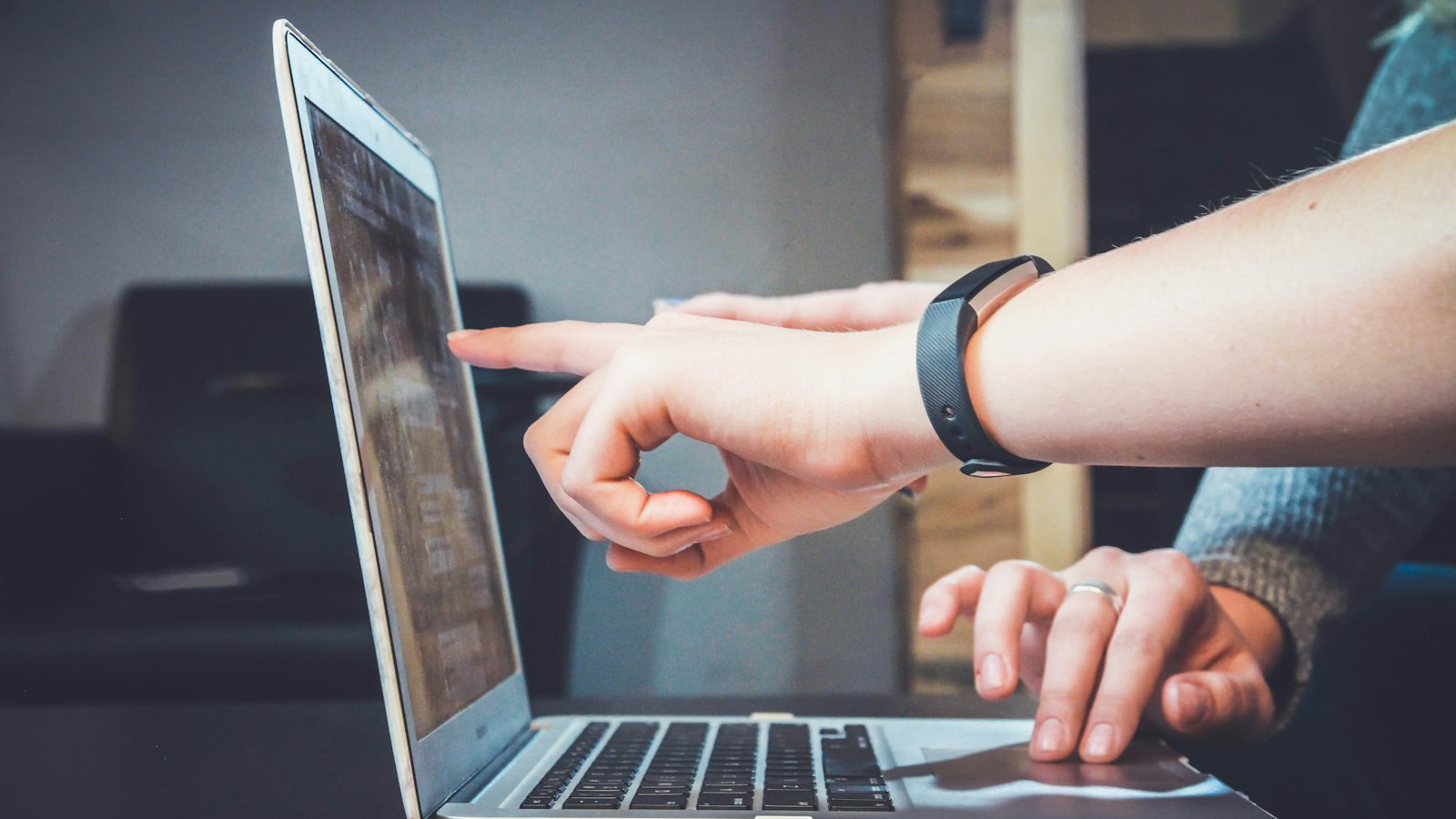 Two people collaborating at a silver laptop on a dark desk