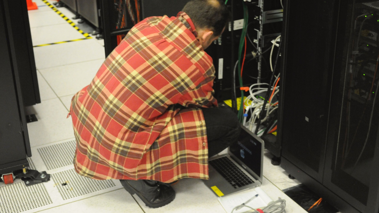 Technician kneeling with a laptop while working on cabling in a data-center server rack