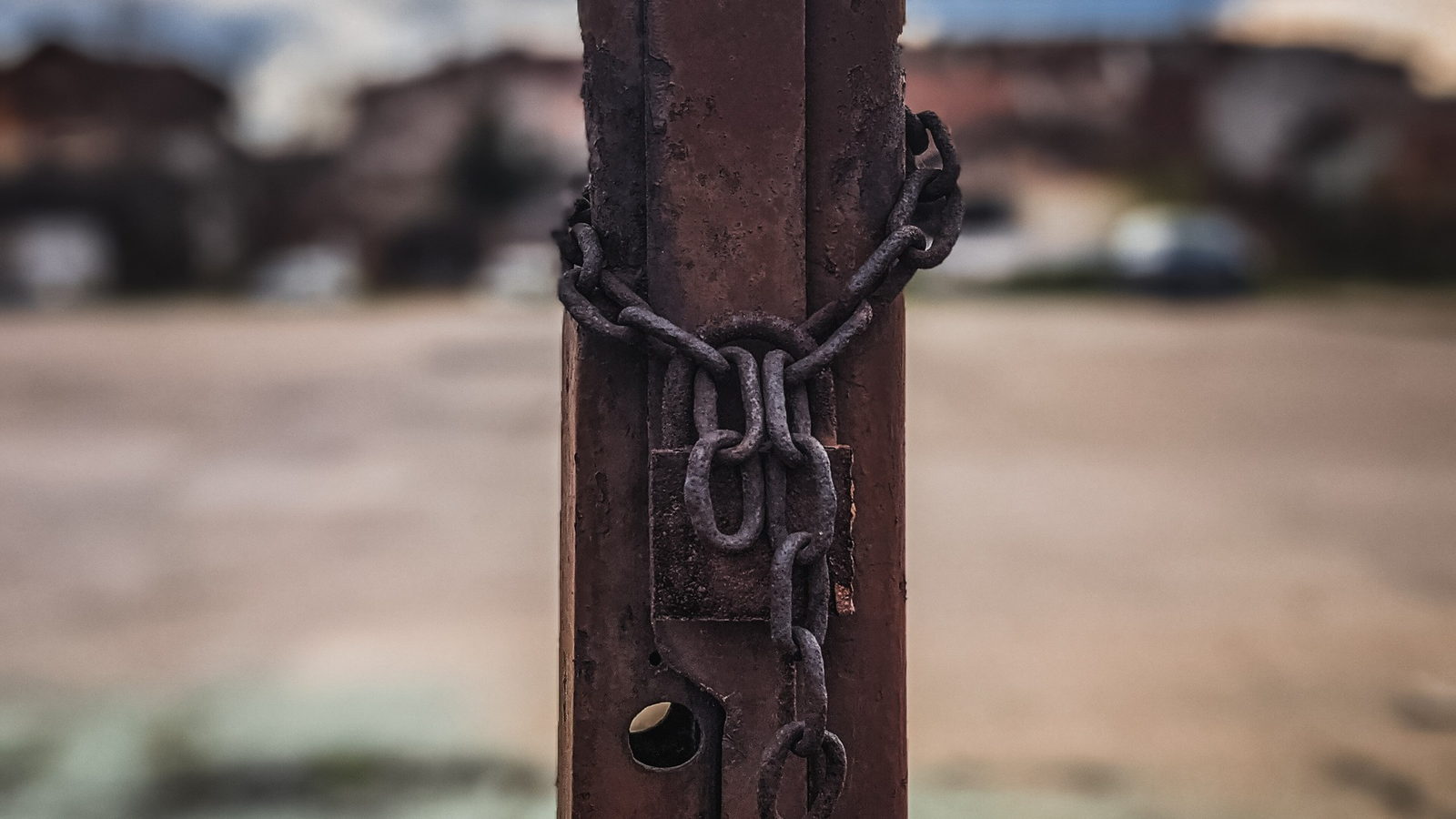 Rusty chain wrapped around a weathered metal post against a blurred background